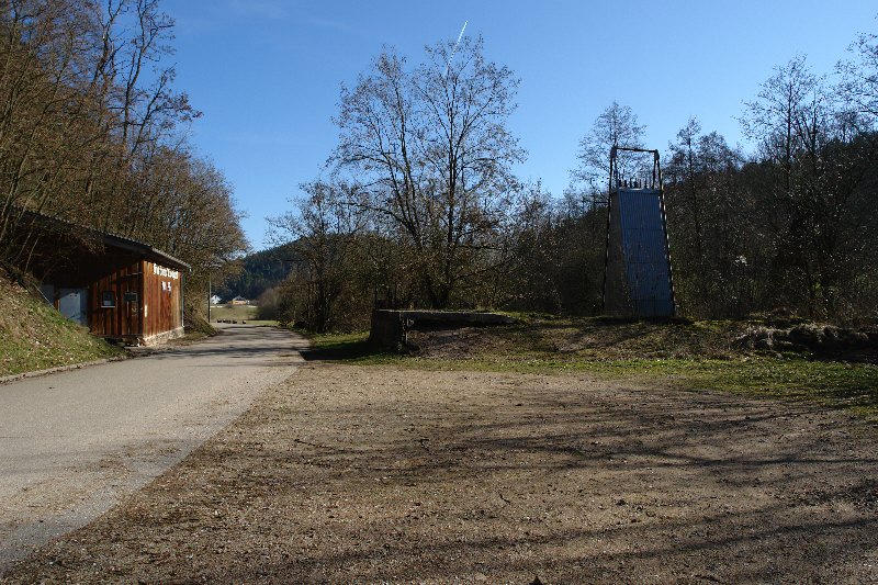 Links der Straße befindet sich die Kaue des Besucherbergwerks, das von der Aktion nicht betroffen war. Rechts sieht man das Gelände, daß geräumt wurde. Im Vordergrund befand sich einst die  Halde, während die Verladerampe und die Trafostation noch zu sehen sind. Dahinter folgt, dicht verwachsen, das Betriebsgelände mit den Aufbereitungsanlagen und dem &quot;Wiesenstollen&quot;.